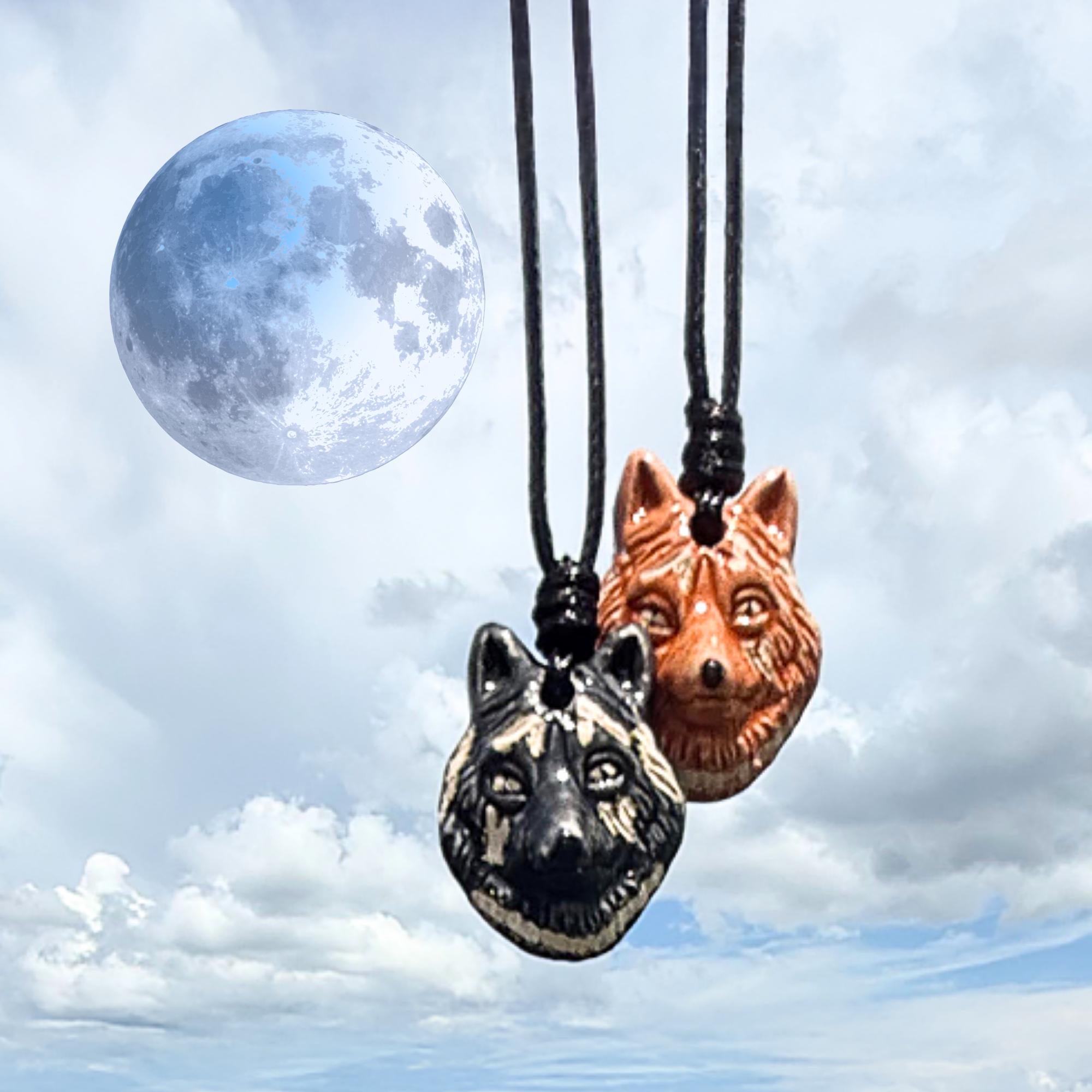 Two wolf-shaped pendants on black cords against a cloudy sky with a full moon.